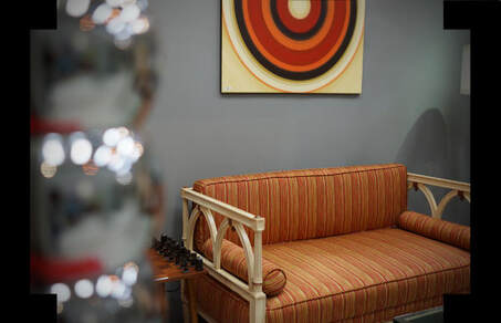 Earth tone stripped upholstered love seat with painted arms below a 1970’s style sunburst wall art with chrome globe accents in the foreground