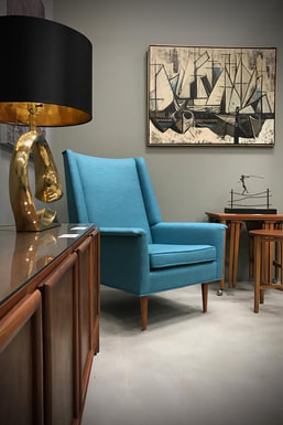Vintage blue upholstered high-back arm chair with stacking side tables and hardwood credenza. Cubist abstract fine art painting on the grey painted wall.